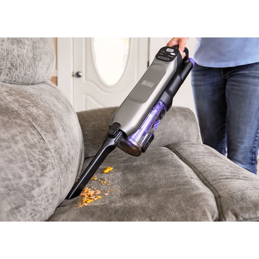 BLACK+DECKER BHFEA640WG handheld vacuum cleaner with slim nozzle cleaning crumbs from a gray sofa.