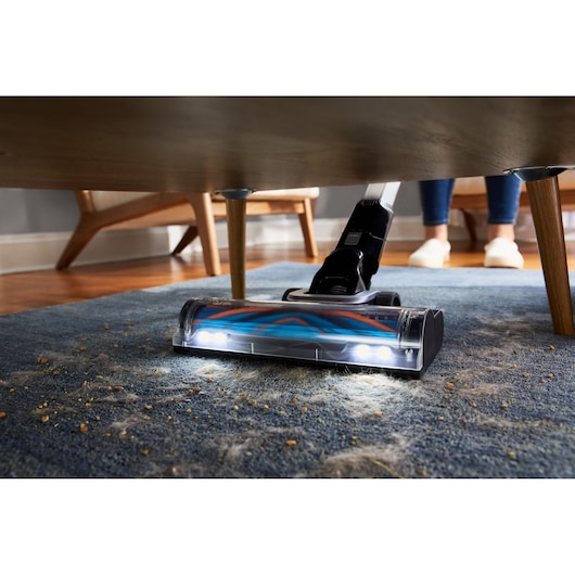 BLACKDECKER BHFEB520D1 cordless vacuum cleaning dirt under table on blue carpet with LED lights, low angle.