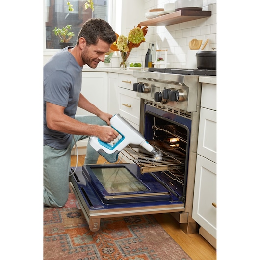 Photo of BLACKDECKER BHSM15FX08 handheld steam cleaner used to clean oven rack in kitchen setting.