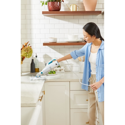 BLACKDECKER BHSM15FX08 steam cleaner used on a kitchen countertop, handheld, in a modern white kitchen.