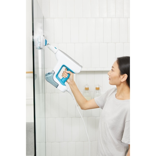 BLACKDECKER BHSM15FX08 steam cleaner in use, cleaning glass shower door with blue and white handheld unit.