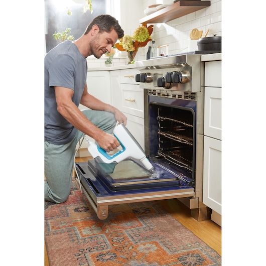 BLACKDECKER BHSM15FX08 steam cleaner used to clean oven door glass in modern kitchen setting.