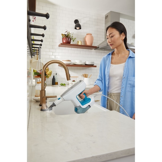 BLACKDECKER BHSM15FX08 handheld steam cleaner with blue accents used to clean a kitchen countertop.