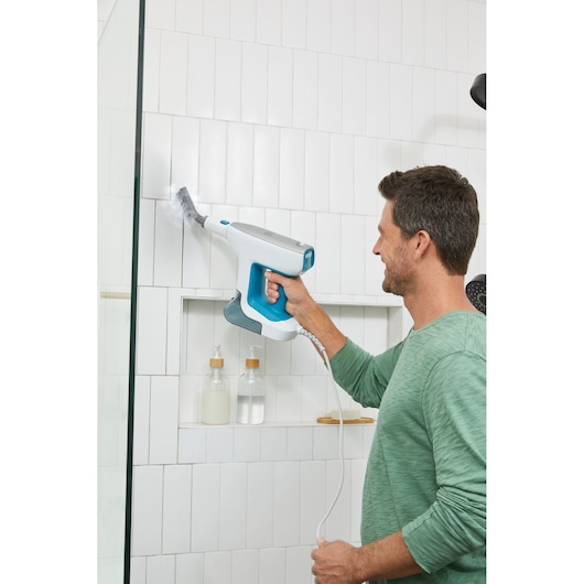 Person using BLACKDECKER BHSM15FX08 handheld steam cleaner to clean white bathroom tiles.