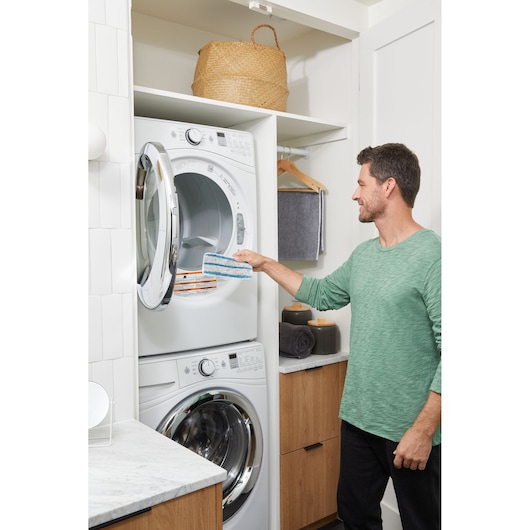 Person using BLACK+DECKER BHSM15FX08 steam mop pad to clean inside a front load dryer in a laundry room.