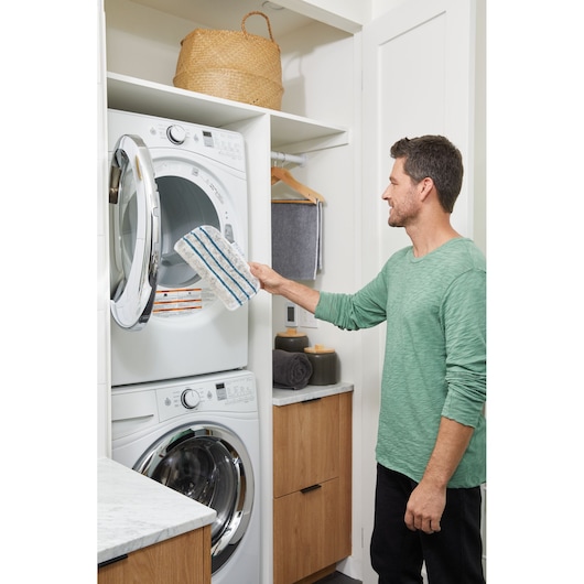 BLACKDECKER BHSM15FX08 steam mop pad in laundry room, man placing pad in front-load dryer.