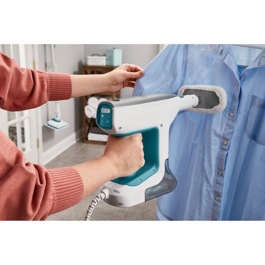 BLACKDECKER BHSM15FX10 handheld steamer used on a blue shirt in a home setting.