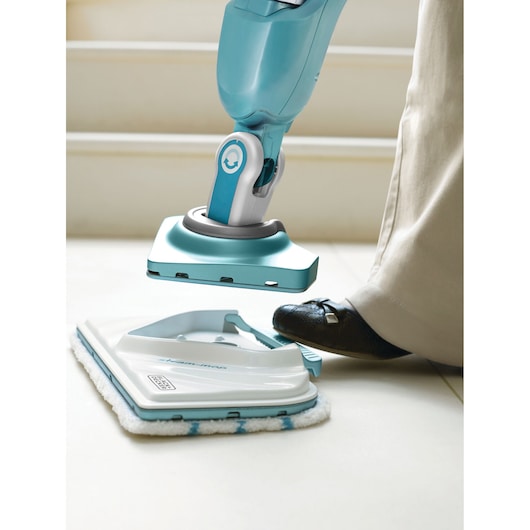 BLACKDECKER BHSM168DSM steam mop head being detached by foot on white tile floor, close-up view.