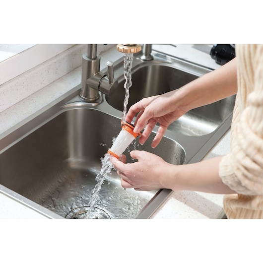 A person rinsing a small cylindrical vacuum filter under running water at a kitchen sink.