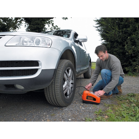 A man inflates a car tyre using the BLACK+DECKER 160 PSI AC/DC Multi Purpose Air Station, with its 3.1 metre DC power cable running through the car window.