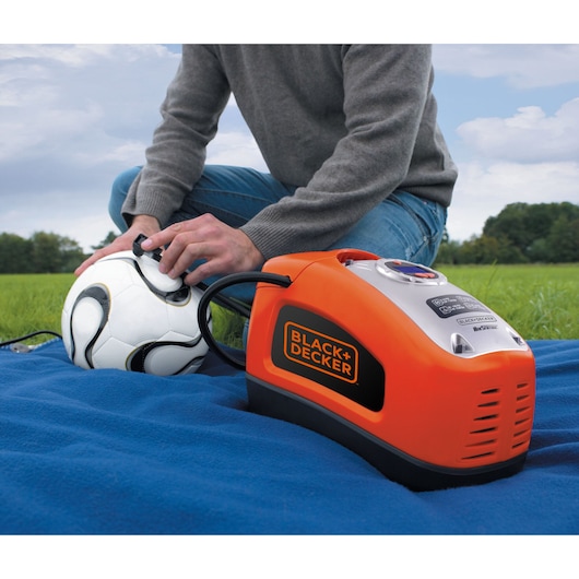 A man inflates a football using the BLACK+DECKER 160 PSI AC/DC Multi Purpose Air Station