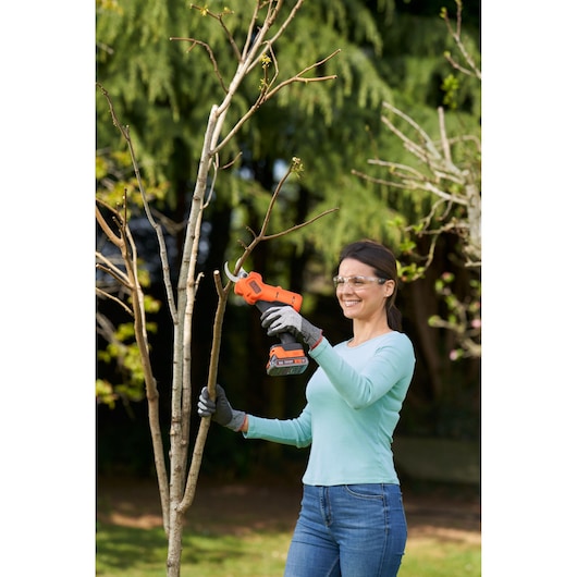 Using BLACK+DECKER 18V Power Pruner outdoors to cut a branch.