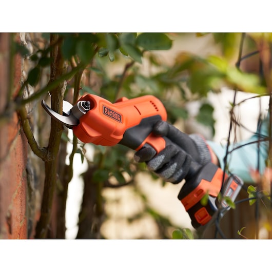Close up of BLACK+DECKER 18V Power Pruner cutting branch close to a wall.