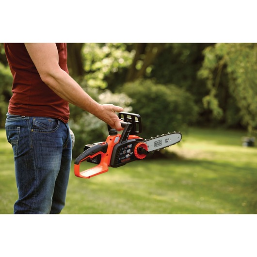 Photo of BLACK+DECKER GKC1825L20 cordless chainsaw with 25cm bar held outdoors in a garden.