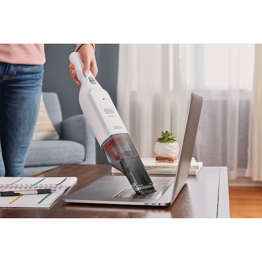 BLACKDECKER HLVC315B11 handheld vacuum cleaning a laptop keyboard on a wooden table in a living room.