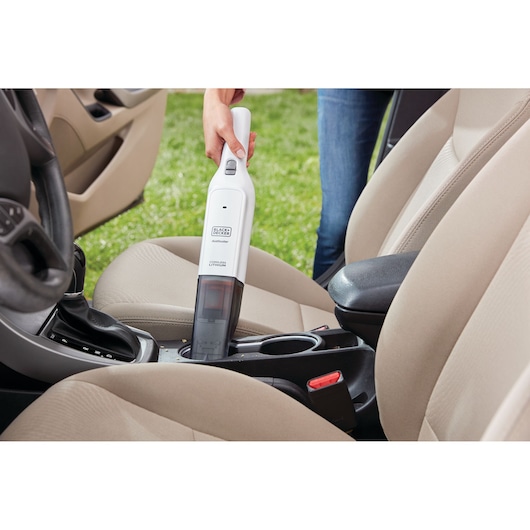 Photo of BLACK+DECKER HLVC315B11 handheld vacuum cleaning beige car seats and console compartment.