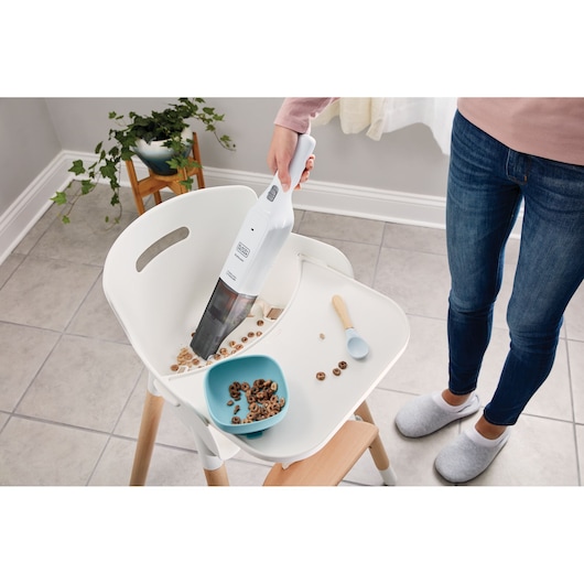 BLACKDECKER HLVC315B11 handheld vacuum cleaning cereal spill on white high chair tray, top view.