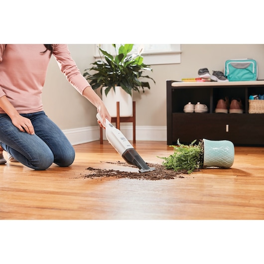 Photo of BLACKDECKER HLVC315B11 handheld vacuum cleaning spilled soil from a knocked over plant on hardwood floor.