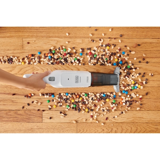 BLACKDECKER HLVC315B11 handheld vacuum cleaning assorted snacks from hardwood floor, top view.