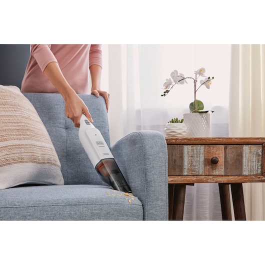 BLACK+DECKER HLVC315B11 handheld vacuum cleaning crumbs from a blue fabric sofa in a living room.