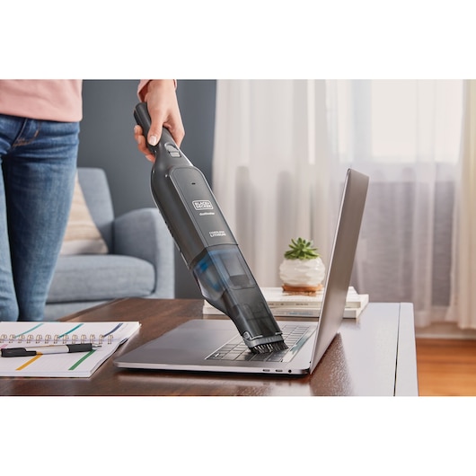 BLACKDECKER HLVC320B11 handheld vacuum cleaning laptop keyboard on desk in living room.