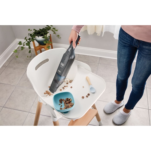 BLACKDECKER HLVC320B11 handheld vacuum cleaning spilled cereal from a high chair tray in a modern kitchen.