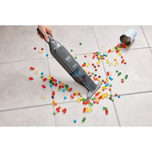 Photo of BLACK+DECKER HLVC320B11 handheld vacuum cleaning spilled candy on tile floor.
