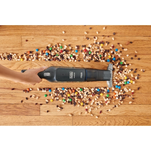 BLACK+DECKER HLVC320B11 handheld vacuum cleaning mixed nuts and candy from a wooden floor, top view.