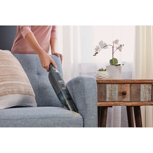 Photo of BLACKDECKER HLVC320B11 handheld vacuum cleaning crumbs from a blue sofa next to a rustic wooden side table.