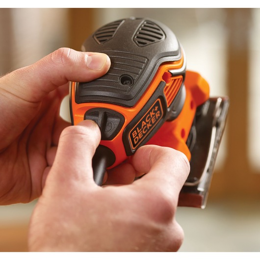 Close-up photo of BLACK+DECKER KA450 detail sander being operated by hand, orange and black body visible.
