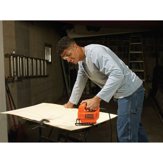 BLACKDECKER KS501 jigsaw cutting plywood on workbench in workshop, orange tool held by user.