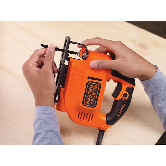 Photo of BLACK+DECKER KS701PEK jigsaw being handled, orange body with black accents, blade visible, on wood surface.