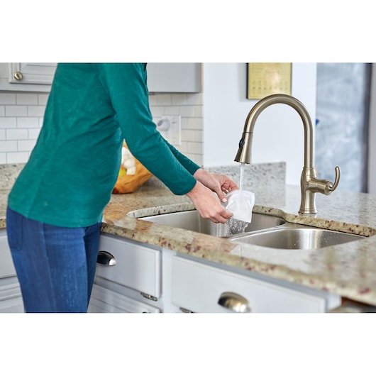 BLACKDECKER NSVA315J vacuum filter being rinsed under kitchen faucet in a home environment.