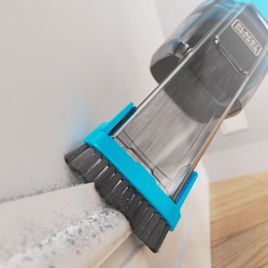 BLACK+DECKER NVD215J handheld vacuum with blue brush attachment cleaning dust from a corner, close-up angle.
