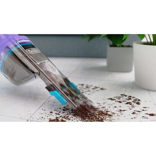 BLACK+DECKER handheld vacuum NVD220BP cleaning dirt on white tile floor near potted plants.