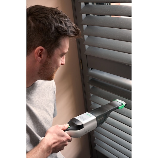Photo of BLACKDECKER REVHV8C handheld vacuum cleaning window blinds indoors.