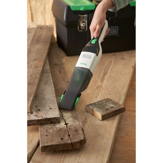 BLACK+DECKER REVHV8C handheld vacuum picking up sawdust on wooden boards near black toolbox.