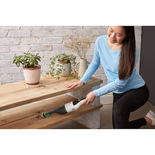 BLACK+DECKER REVHV8C handheld vacuum cleaning dirt from a wooden shelf with potted plants, lifestyle setting.