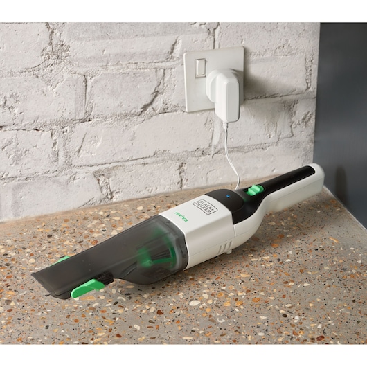 Photo of BLACK+DECKER REVHV8C handheld vacuum in white and black, charging on countertop near a brick wall.