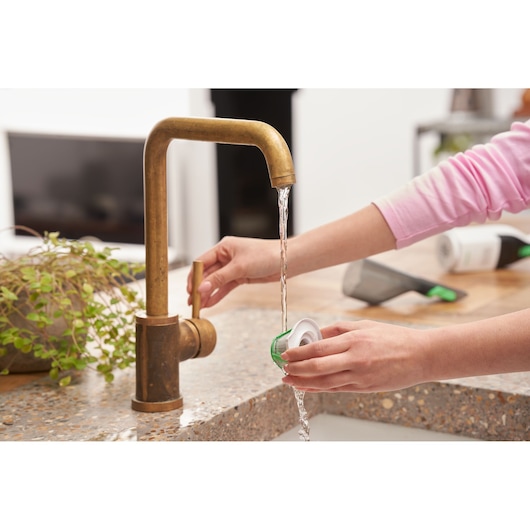 Photo of hands rinsing BLACKDECKER REVHV8C vacuum filter under brass kitchen faucet on countertop.