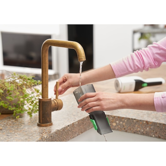 BLACK+DECKER REVHV8C handheld vacuum dustbin being rinsed under kitchen faucet, countertop view.