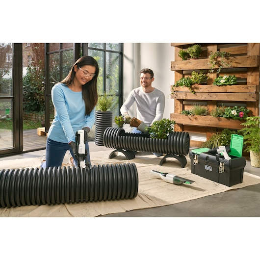 Photo of BLACKDECKER REVHD12C cordless tool used for cutting black ribbed pipe in indoor garden setting.