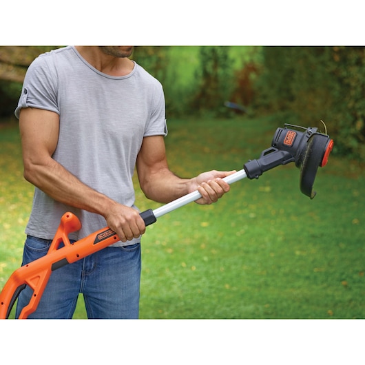 BLACKDECKER ST182320 grass trimmer held outdoors with orange and black design, adjustable shaft.