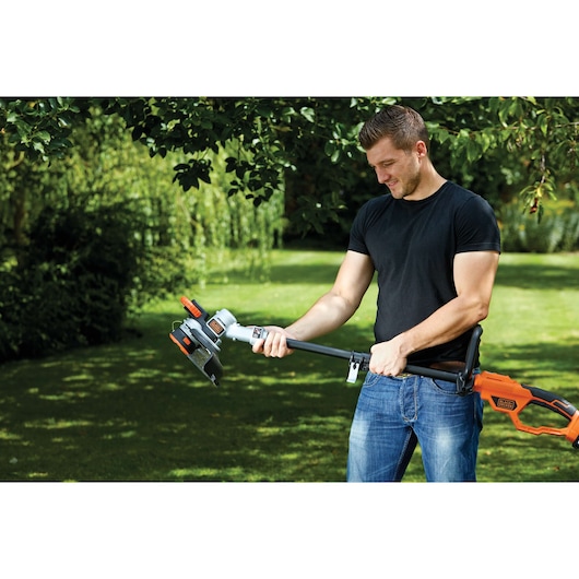 Photo of BLACKDECKER STC1840PC grass trimmer in use outdoors, orange and black design, handheld garden tool.