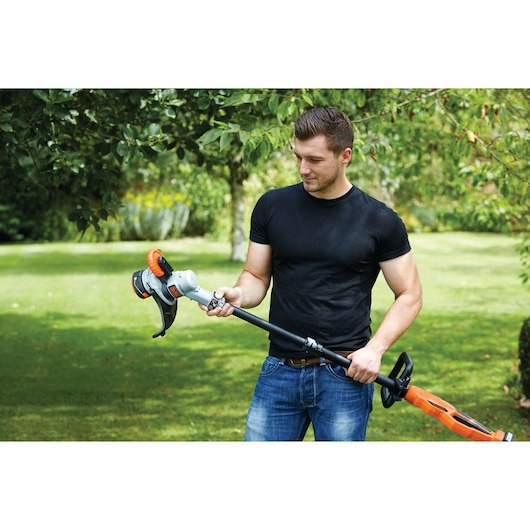 Photo of a person holding a BLACKDECKER STC1840PC cordless grass trimmer in a garden setting.